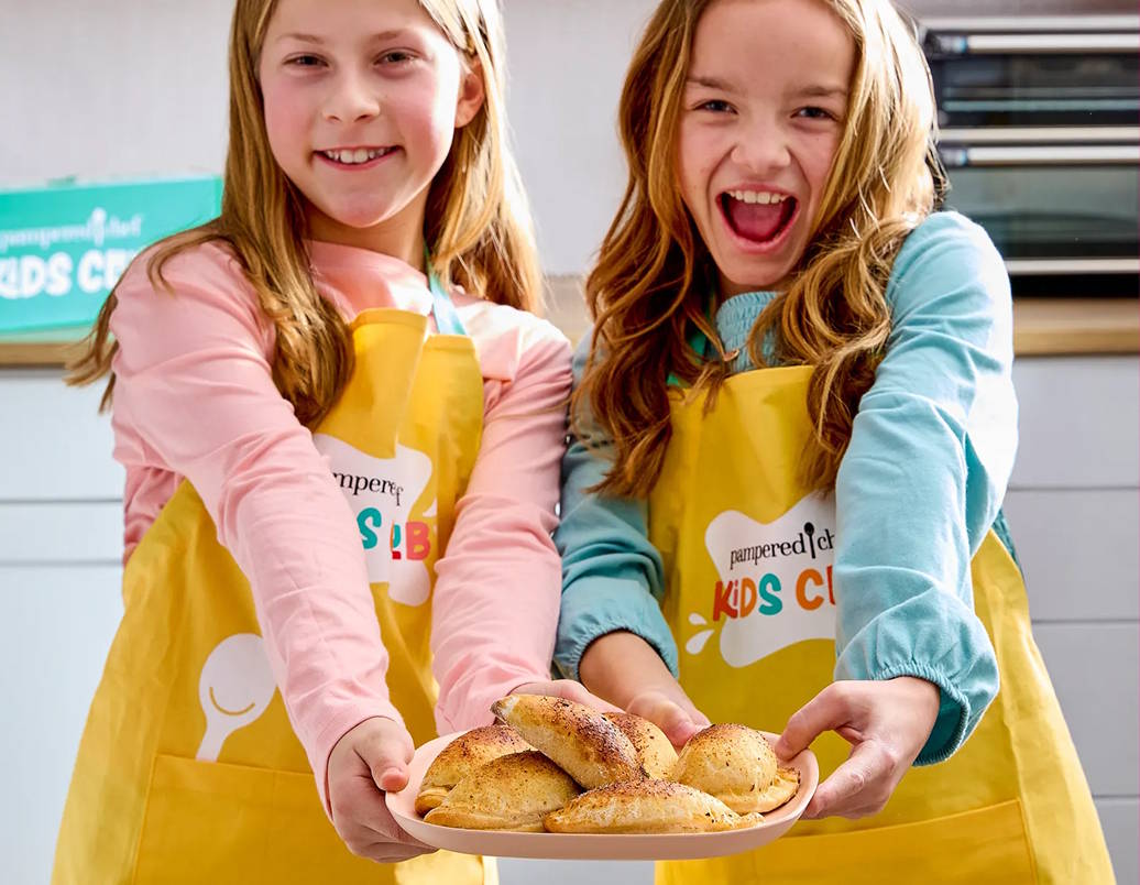 Two yong girls wearing kids club aprons holding a plate of food, together
